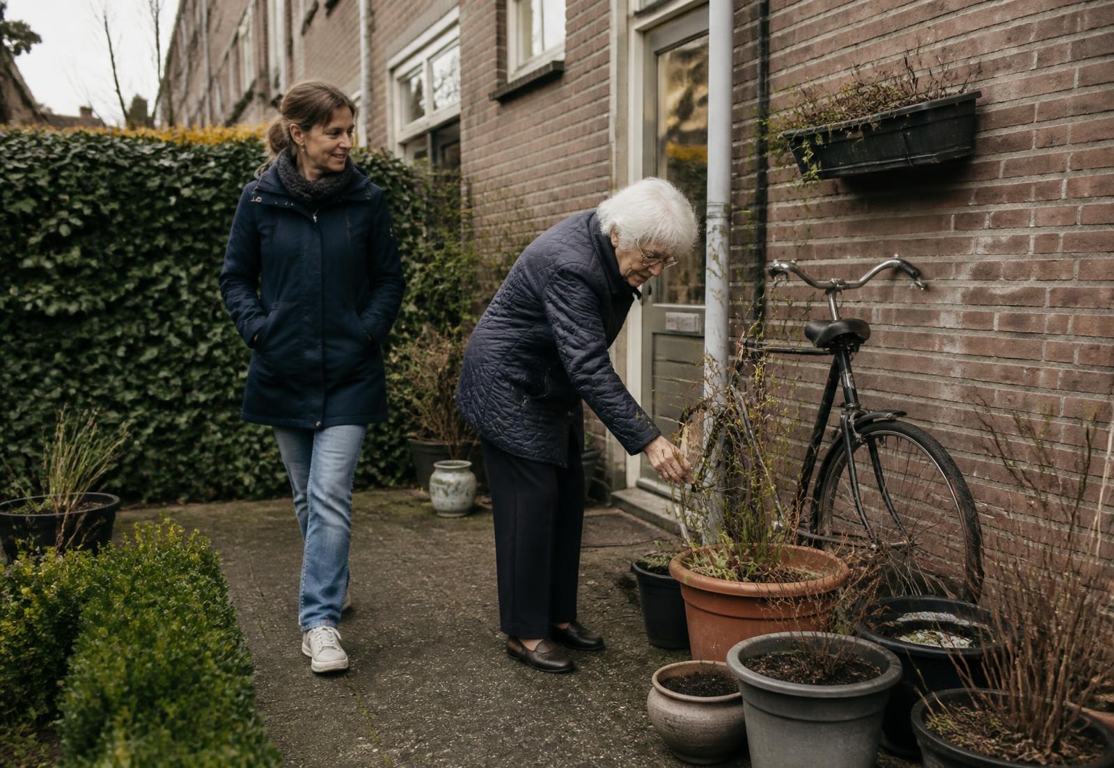 Oudere vrouw verzorgt haar planten in de achtertuin, met een bekende naaste naast haar
